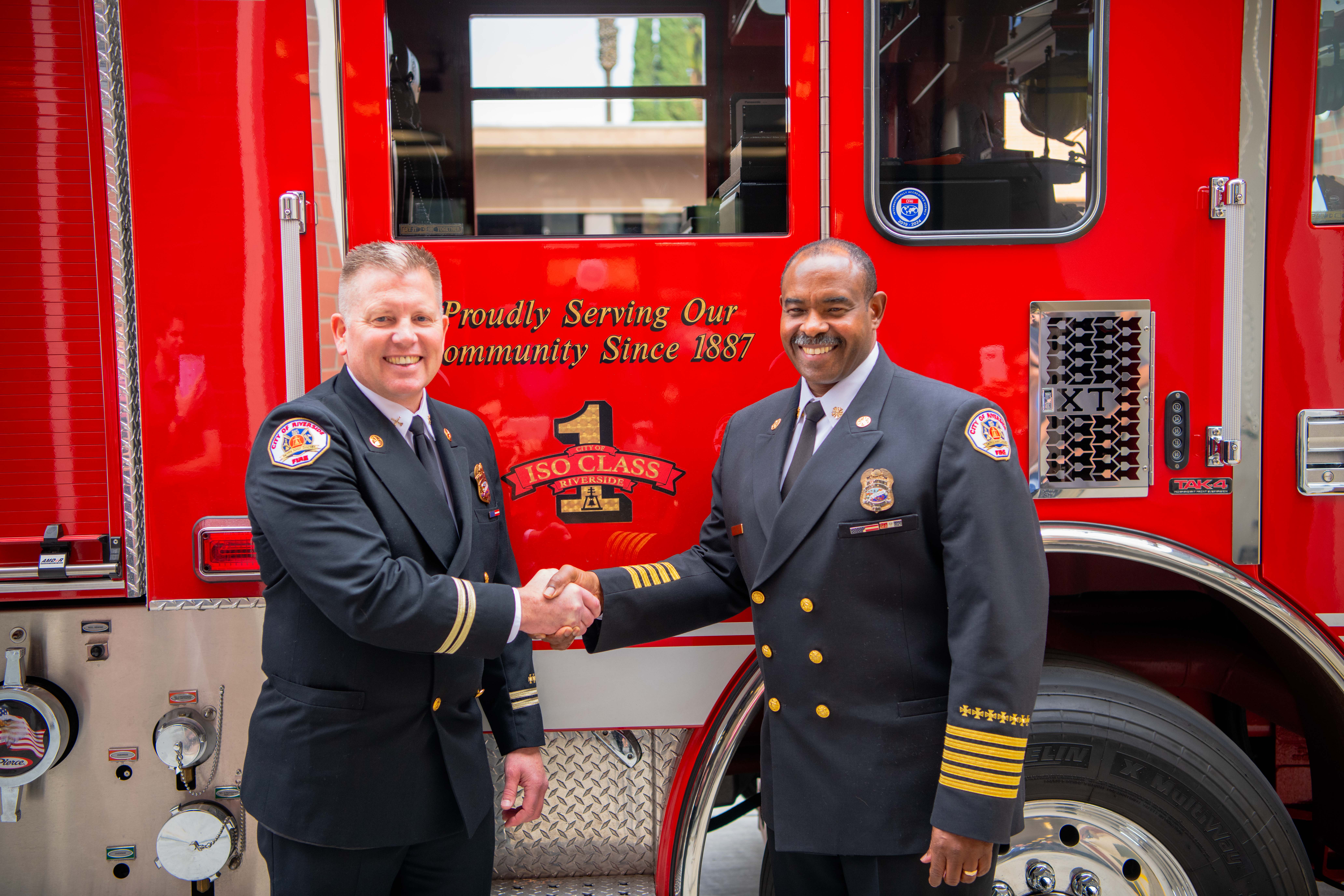 Chief Moore shaking hands in front of a fire engine with Chief Gooch